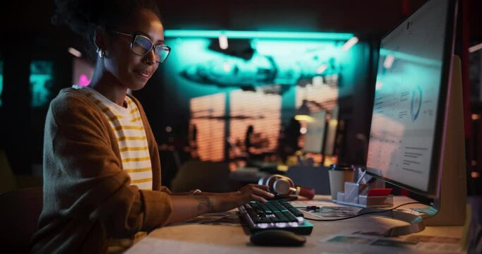 Zoom in: Motivated Black Female Using Desktop Computer in Creative Agency in the Evening. Happy Dedicated Woman Working in a Creative Job Position in an Advertising Company While Smiling