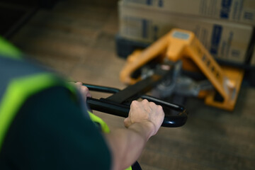 Unrecognizable male warehouse worker pulling a pallet truck with boxes