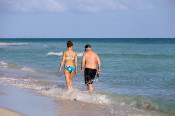 Couple walking by the sand on sea waves background. Sunny beach with tourist resort