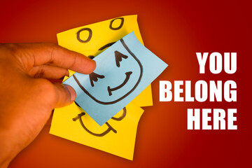 hand holding smiling yellow sticky note, symbol of belonging and inclusion. Business, inclusion and ownership concept.