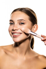 Beauty portrait of an half naked woman holding set of make-up brushes and winking over white background