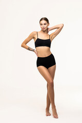 Fototapeta premium Full-length portrait of young slim woman posing in black underwear isolated over grey background.