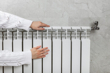 Home central heating system. Women's hands on a radiator against a light wall. A man warms his...