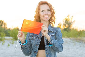 Young woman 25 - 30 years old with the flag of China against a background of nature. Red haired girl in a denim jacket.