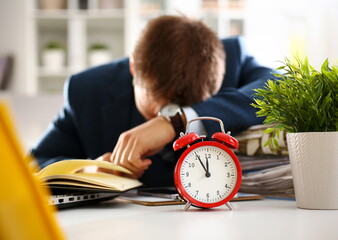 Red alarm clock shows late time closeup and tired office male clerk in suit take nap on table...
