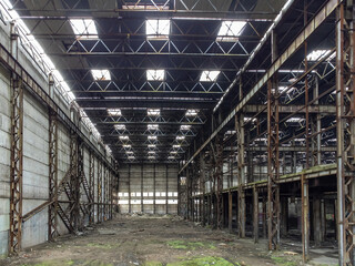 Bankrupt manufactory. Empty industrial enterprise. Manufactory after closing. Industrial hangar with rusty metal structures. Abandoned industrial plant. Bankrupt plant with mold and litter on ground