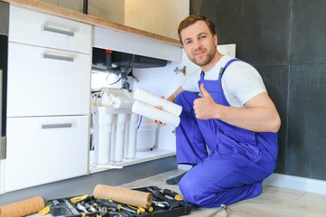Plumber installs or change water filter. Replacement aqua filter. Repairman installing water filter cartridges in a kitchen. Installation of reverse osmosis water purification system. - obrazy, fototapety, plakaty
