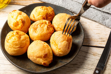 man picking up brazilian pão de queijo with a fork, or cheese breads in a dark plate, fresh homemade gourmet cheese buns