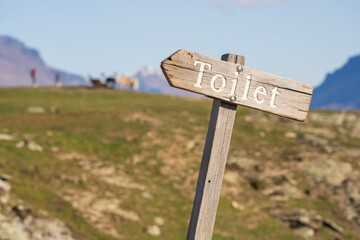 Outdoor toilet sign in grassland and mountains. Rustic wooden sign with the word Toilet