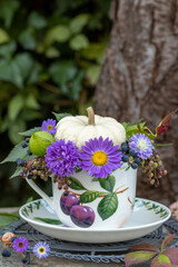 florales Arrangement mit weißem Kürbis Baby Boo und lila Asterblüten in einer Tasse