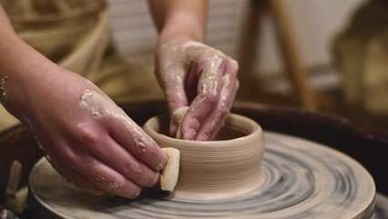 Potter girl works on potter's wheel, making ceramic pot out of clay in pottery workshop. Art and hobby concept. slow motion