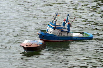 A small radio-controlled fishing boat is towed by a RC patrol ship