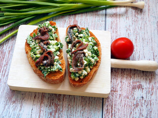 Delicious sandwiches with cream cheese, anchovies and herbs and tomato on white wooden table