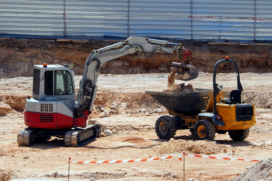 Mini excavator or backhoe and small truck move in the construction site for building