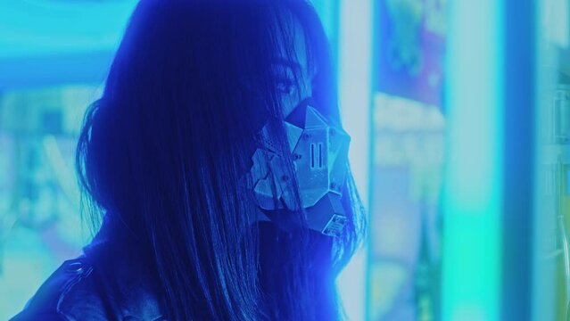 Asian woman wearing a cyberpunk mask amidst the lights stands looking at the camera 