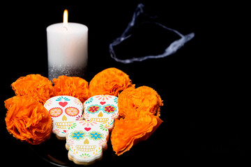 Cookies with shapes of Mexican catrinas and flowers with candle to celebrate Halloween or Day of the Dead on black background