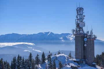 Tower of telecommunication with many antennas on top of Postavaru mountains (Brasov, Romania), in a beautiful winter mountains landscape, with Bucegi mountains in background and clear blue sky