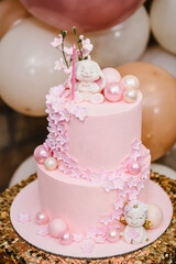 Birthday cake for 1 year on golden table. Pink cake is decorated with rabbit figure and flowers decor for girl. Delicious reception at a birthday party. Trendy cake on background of balloons. Closeup