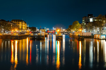 Fototapeta na wymiar Illuminated Canals and Riverside Delights: Exploring Amsterdam After Dark. Captivating Cityscape of Amsterdam at Night: A Delightful Blend of Tradition and Modernity