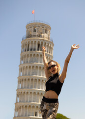 Happy young woman with her hands raised in front of the Leaning Tower of Pisa.