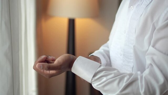 Elegant man getting dressed in the room. Groom buttoning his white shirt during his preparations for the wedding.