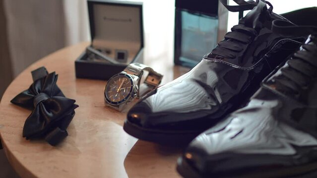The groom's wedding shoes. Wedding, preparations for the wedding. Table with clock, perfume, bow tie and cufflinks.