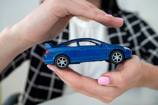 Closeup of female hands for protection small toy car at office