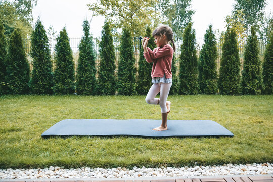 Cute little girl 5-6 years old standing in the Eagle position or Garudasana while practicing yoga outdoors