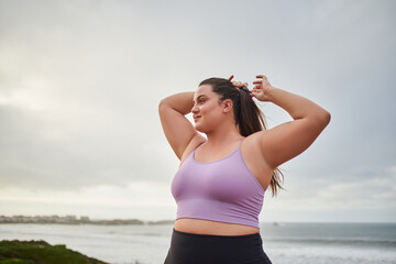 Relaxed smiling woman looking away and correcting hair while walking at the sea