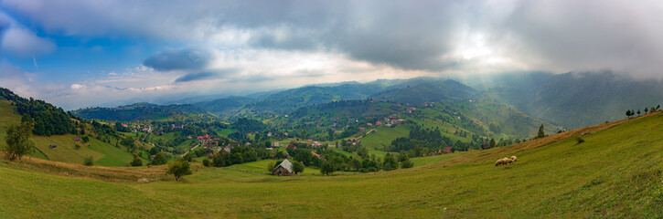 Rural idyllic landscape of the small villages in the Rucar-Bran mountain area, Brasov, Romania, scattered on the wooded hills, with the Bucegi mountains in the background, in wonderful springtime day