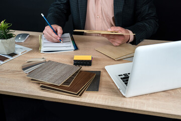 Designer hand choosing wood texture laminate  in catalog at office desk, laptop pen and notepad