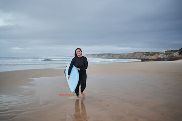 Fototapeta na wymiar Happy european body positive girl on her way to the ocean with surfboard