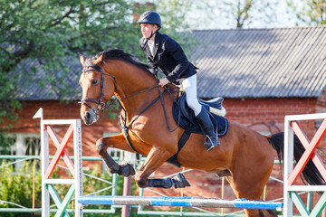 Young sportsman riding horse bounding over obstacle on showjumping competition