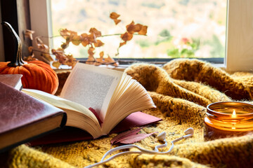 Audiobook or podcast in fall season. Open book with headphones and autumn leaves on knitted plaid...