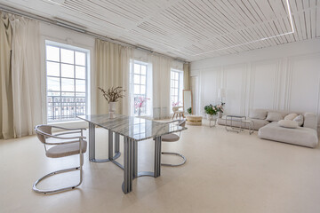 marble dining table and two chairs against the backdrop of a panoramic window into the interior of a bright living room in a luxurious Baroque style with white walls decorated with antique stucco