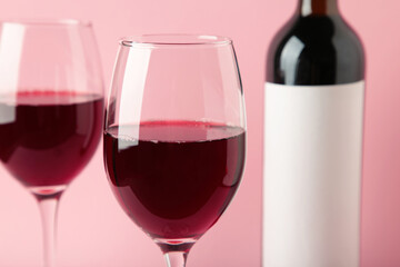 Red wine bottle and wine glass on pink background.