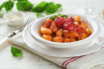 Potato gnocchi. Traditional homemade potato gnocchi with tomato sauce, basil and parmesan cheese on kitchen table on light grey kitchen table background. Traditional Italian food. Top view.