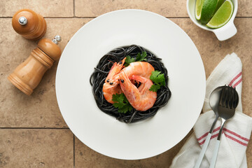 Black spaghetti pasta shrimp on black plate on light concrete table background. Squid ink pasta with prawns. Pasta seafood. Top view on black stone table. Mediterranean traditional cuisine dish.