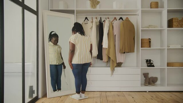 Black Woman Exited about Weight Loss. Cheerful African overweight female dancing at home. 20s plus size woman trying to loose weight.