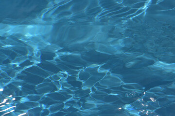 Blue water with ripples on the surface. Defocus blurred transparent blue colored clear calm water surface texture with splashes and bubbles. Water waves with shining pattern texture background.