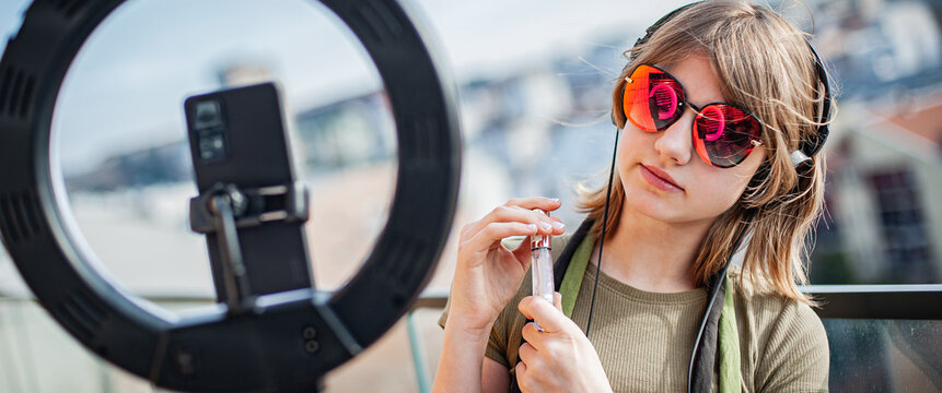 Influencer young woman recording video on smartphone and lighting herself with ring lamp. Broadcast communicates with followers in social networks.