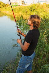 a young man in a black T-shirt and glasses with a cigarette fishing on the river