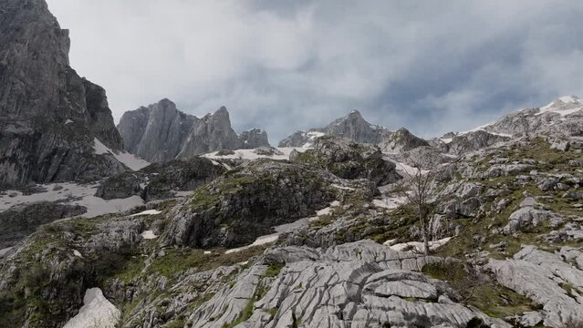 rocky mountain landscape, summer sunny day. ridges with a white snow. close and low flight over the stones, establishing shot