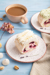 Roll biscuit cake with cream cheese and jam, cup of coffee on blue wooden, side view.