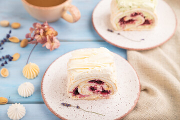 Roll biscuit cake with cream cheese and jam, cup of coffee on blue wooden, side view, selective focus.