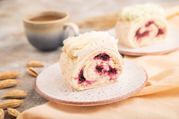 Roll biscuit cake with cream cheese and jam, cup of coffee on brown concrete, side view, selective focus.