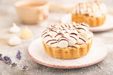 Two tartlets with meringue cream and cup of coffee on brown concrete, side view, selective focus.