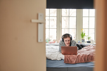 Attractive young teenager wearing headphones working on laptop computer at home