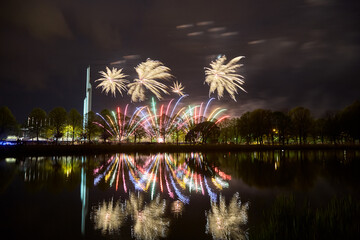 Brightly colorful fireworks and salute of various colors in the night sky, reflecting in water, in park.