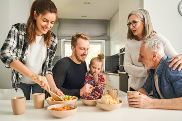 Multi-generation family preparing breakfast together in light kitchen